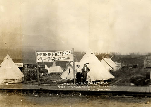 Two men stand in front a tent and a sign reading Fernie Free Press
